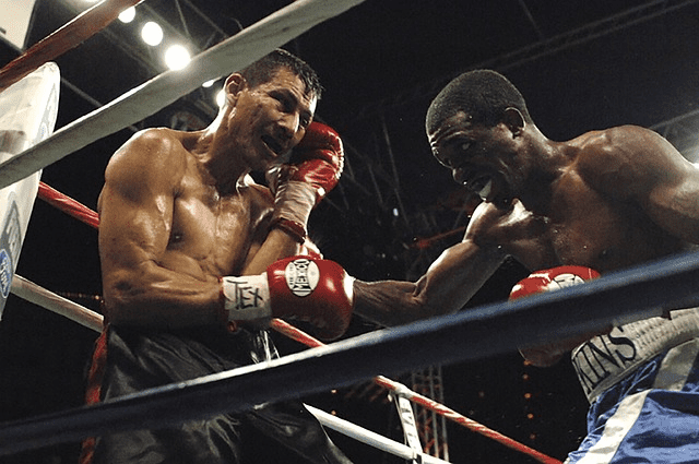 A boxer hitting another one with a right hook, in a ring corner, during a boxing match